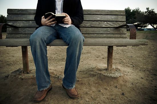 Man on bench reading Bible