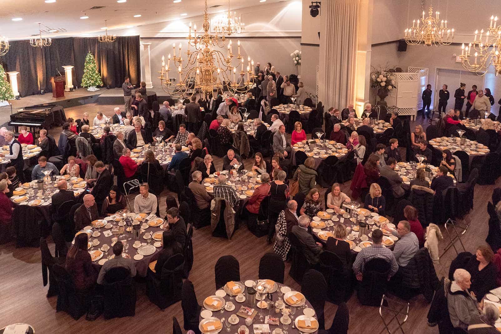 An image of guests sitting down at over a dozen tables across a large gala room.