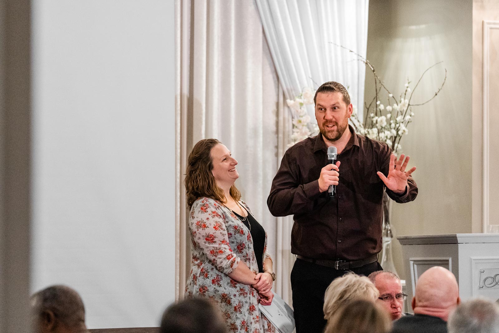 A man and a woman stand together on stage, smiling and laughing.